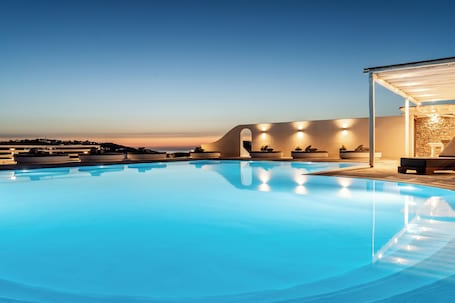 A swimming pool with a view of the sunset, lounge chairs, and a covered seating area.