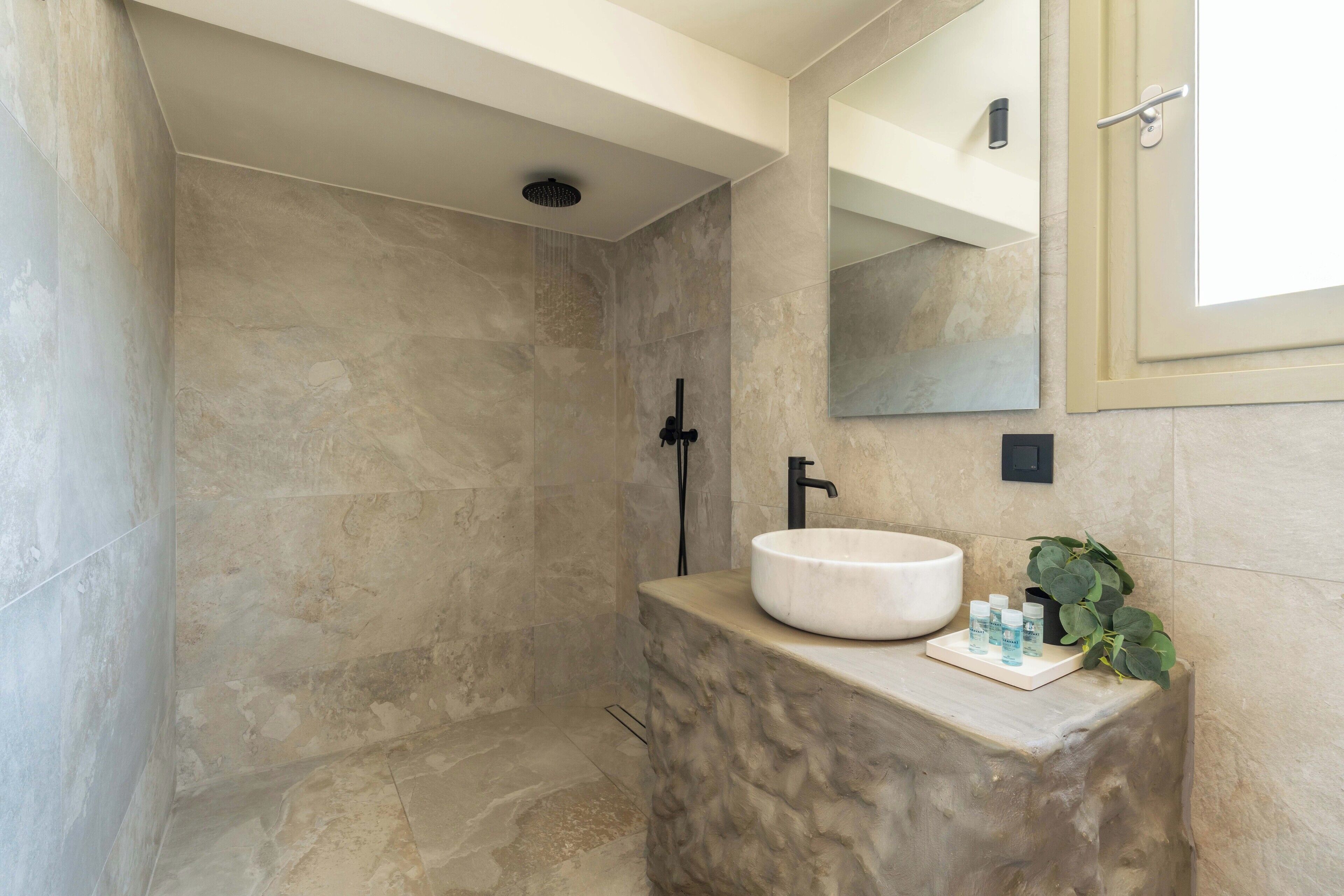 A modern bathroom with a stone shower, a white sink, and a mirror above it.