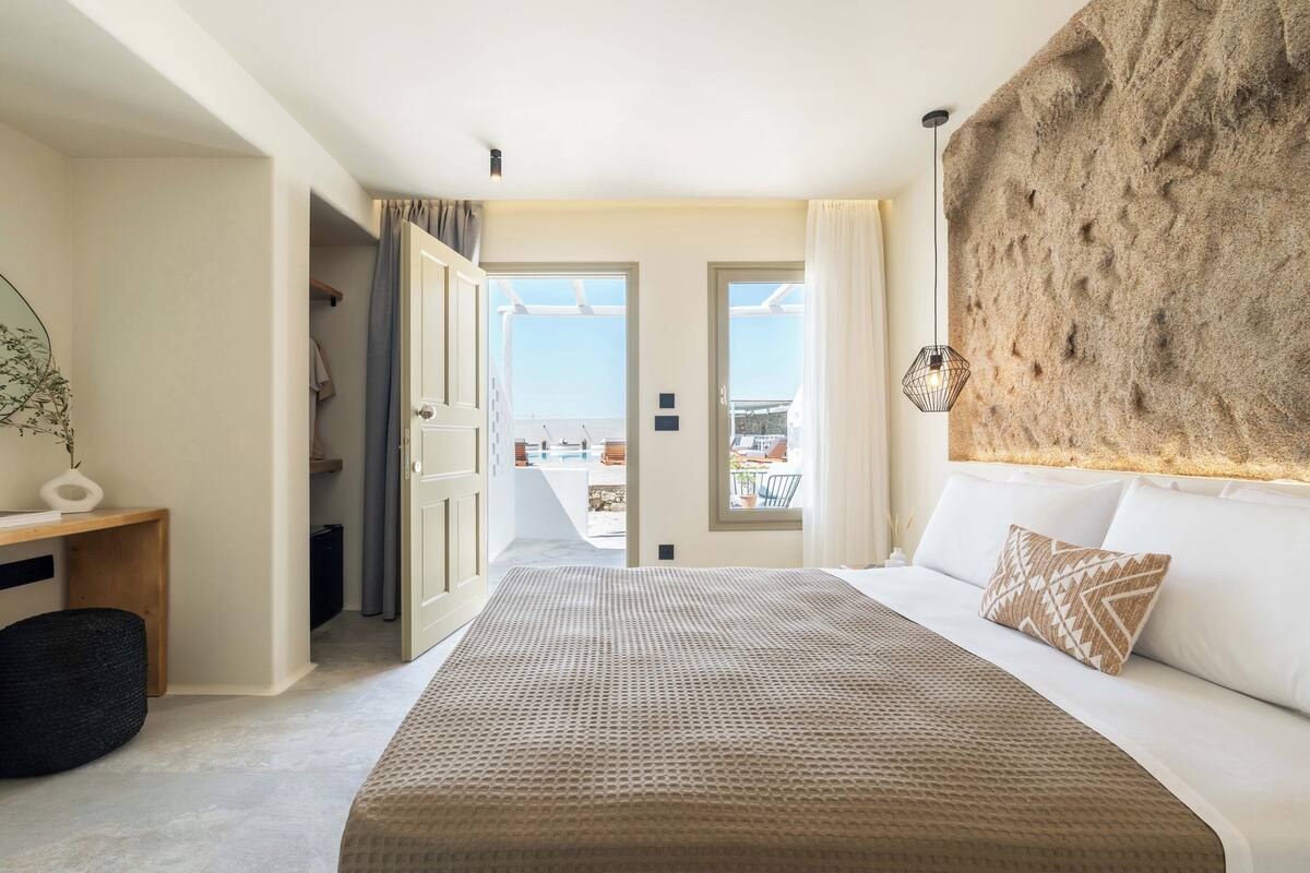 A bedroom with a large bed, a view of the outdoors, and a textured wall.