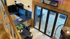 Ett rymligt vardagsrum i loftstil med en trätrappa, ett matbord med stolar, en soffa och en stor skjutdörr i glas som leder ut till en uteplats.