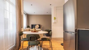 Ein modernes Wohnzimmer mit einem runden Esstisch, vier Stühlen, einer Couch, einem Flachbildfernseher und einem eingebauten Kühlschrank.