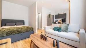 Ein modernes Hotelzimmer mit Bett, Sofa, Couchtisch aus Holz und einer Küche im Hintergrund.
