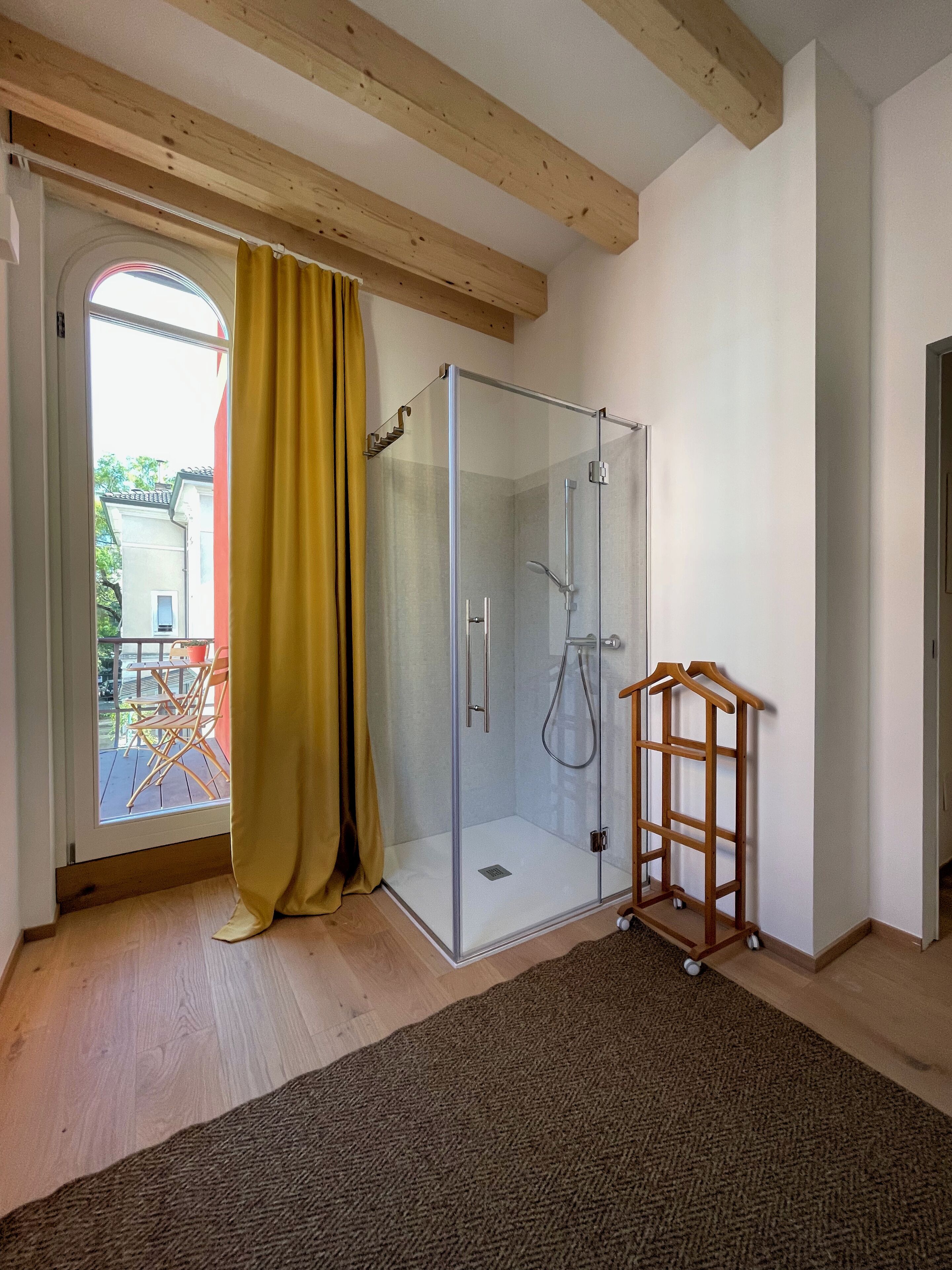 A glass-enclosed shower room with a wooden ceiling, a yellow curtain, and a wooden drying rack.
