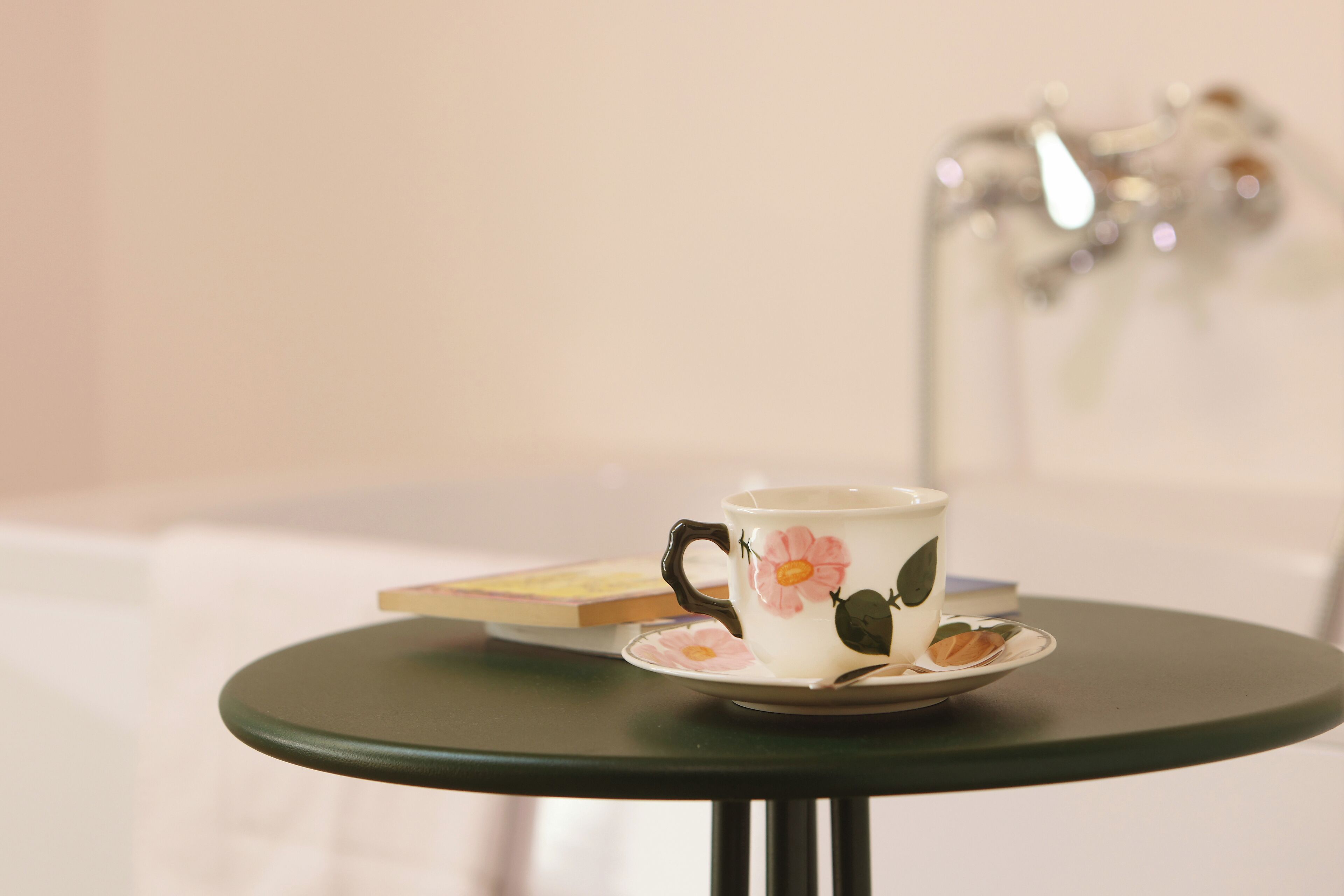 Un tavolino con una tazza e un piattino floreali, un libro e un oggetto decorativo sullo sfondo.