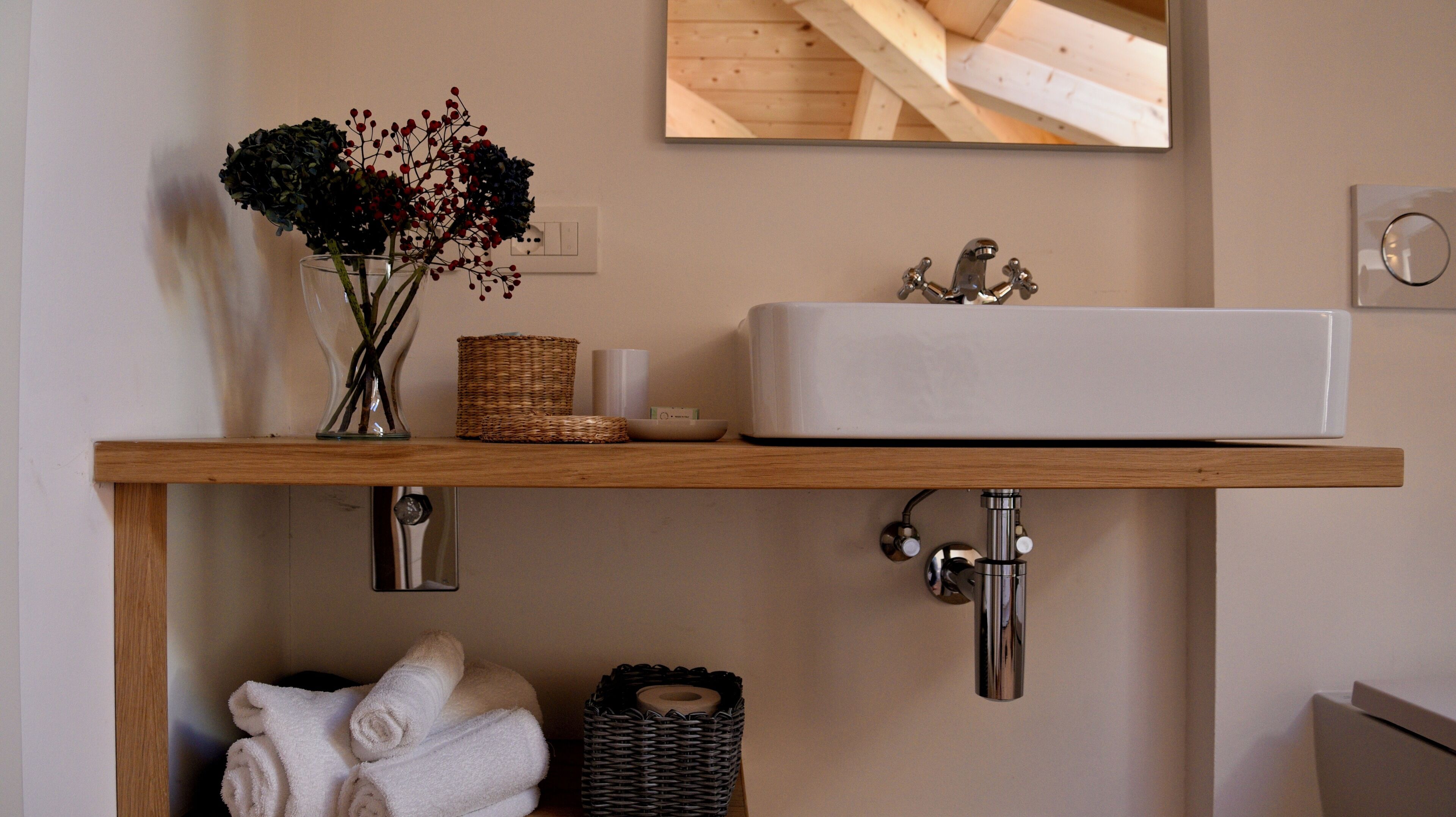 A bathroom with a wooden shelf holding a vase with flowers, a soap dish, and a basket.