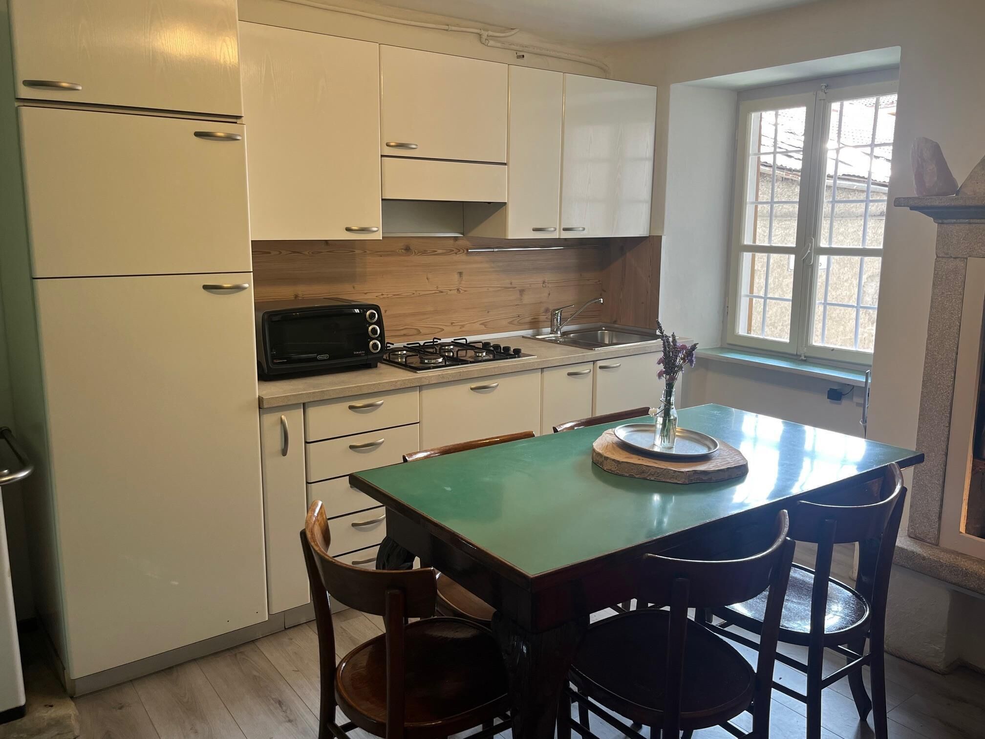 Una cocina con armarios blancos, una mesa verde y dos sillas de madera.