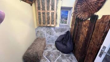 Un banco de piedra con diseño en forma de corazón, un sillón de cuero negro y un fardo de heno en una habitación rústica con una puerta de madera y una ventana con vistas a la montaña.