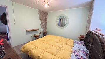 A bedroom with a bed, a wooden headboard, a stone accent wall, a round mirror, and a hanging light fixture.