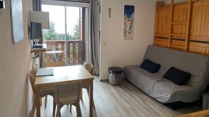 Uma sala de estar aconchegante com sofá, uma mesa de jantar com cadeiras, televisão e varanda com vista.
