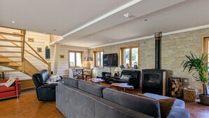 A spacious living room with a large grey sofa, a TV, a fireplace, and a staircase leading to an upper level. - Spacious family chalet with spa, sauna and games room (Ban-sur-Meurthe-Clefcy)