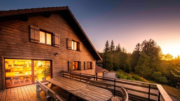 A wooden cabin with a deck, a dining area, and a view of the surrounding forest. - Spacious family chalet with spa, sauna and games room (Ban-sur-Meurthe-Clefcy)