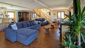 A spacious living area with a large blue sectional sofa, a wooden staircase, and a dining table with chairs. - Spacious family chalet with spa, sauna and games room (Ban-sur-Meurthe-Clefcy)