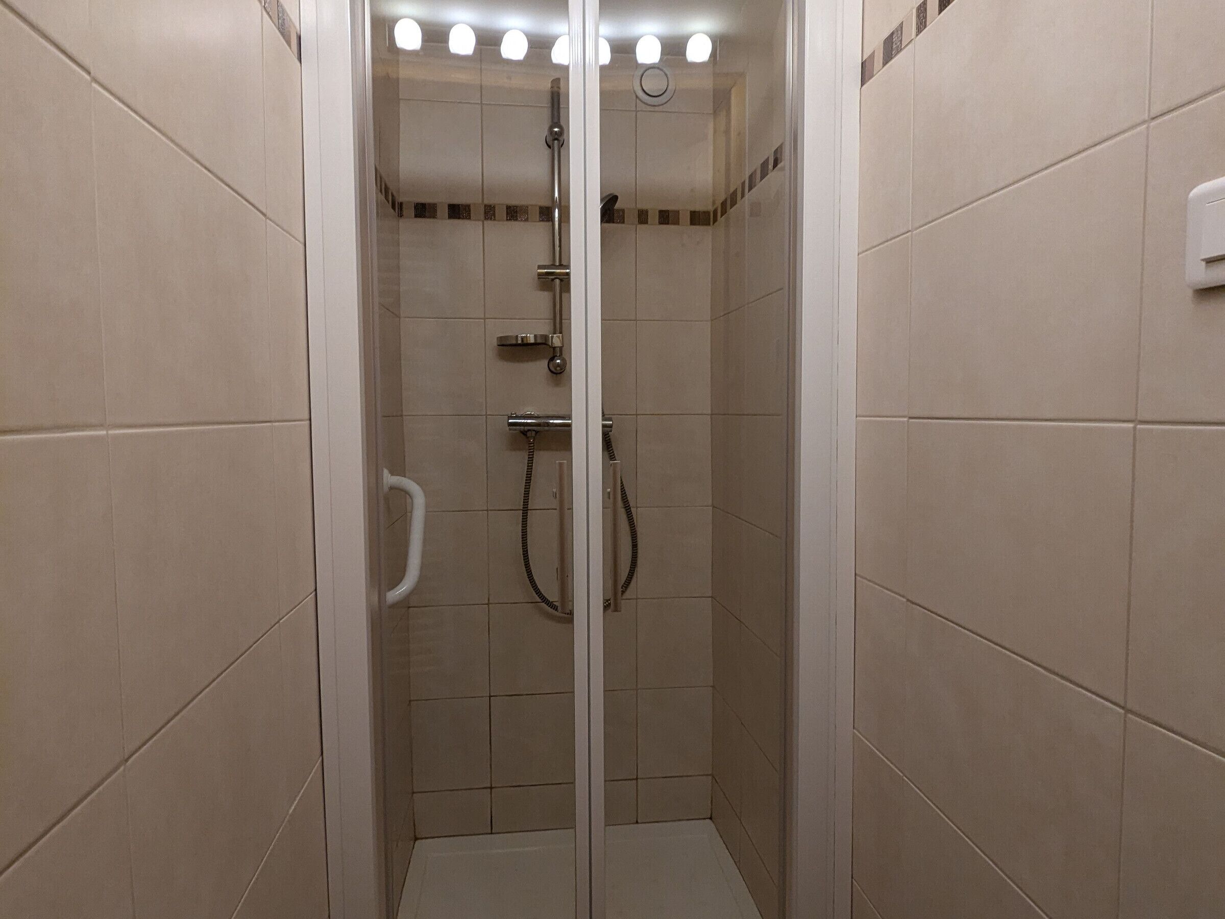 A walk-in shower with a glass door, tiled walls, and a handheld showerhead.