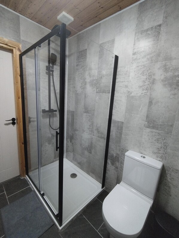 A bathroom with a glass-enclosed shower, a white toilet, and grey tiled walls.