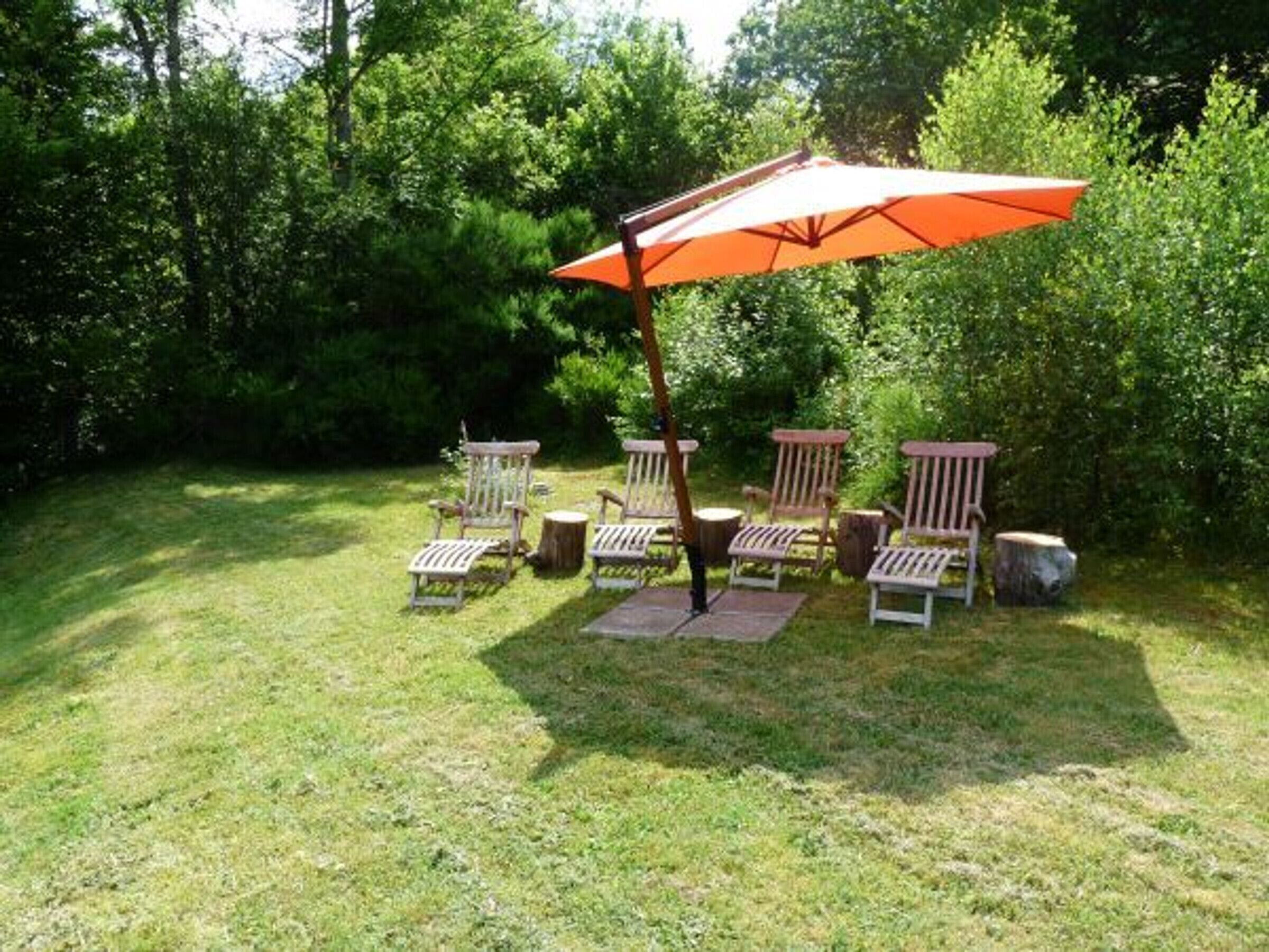A patio area with wooden chairs and a large orange umbrella.