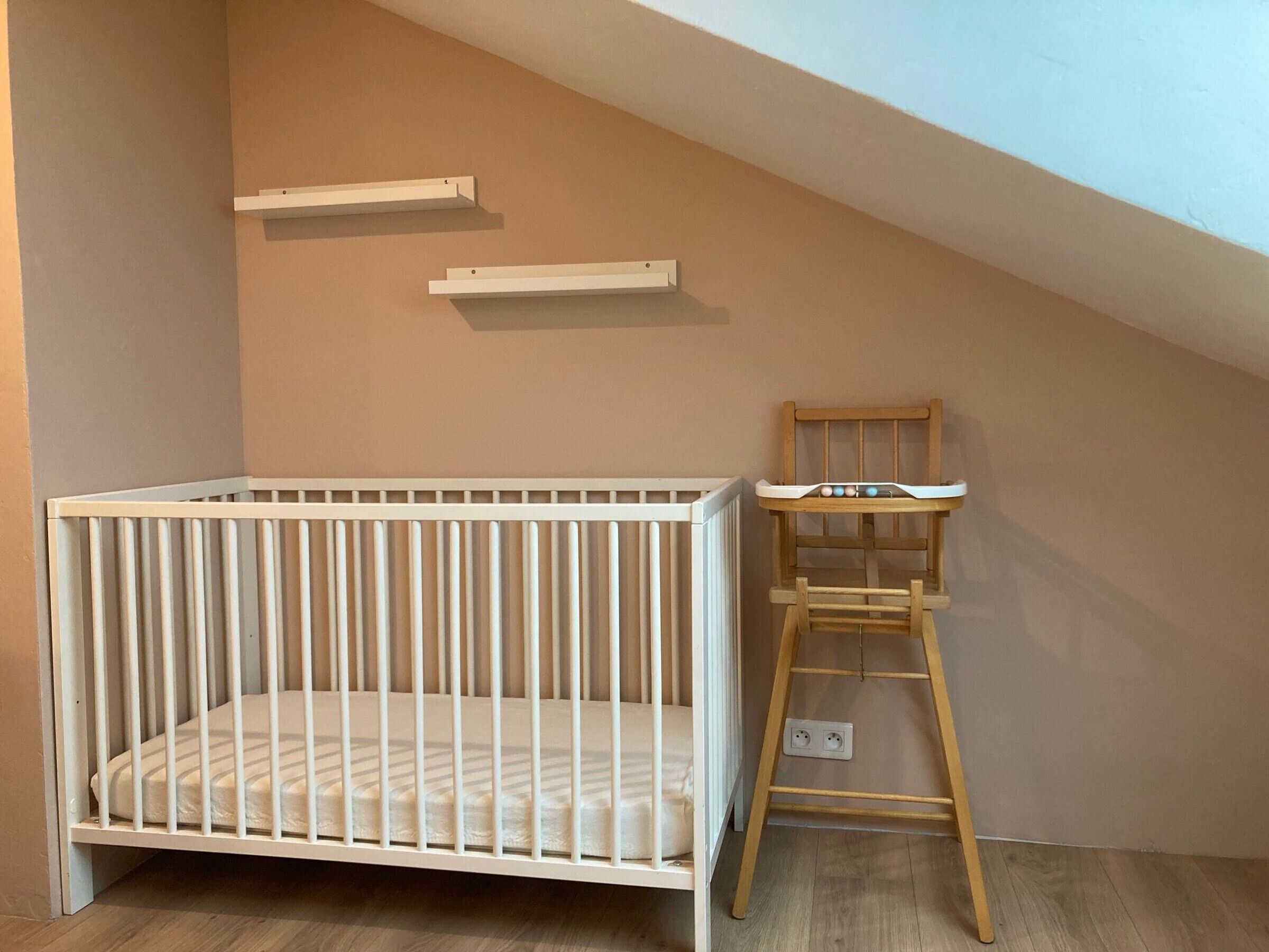 Un berceau blanc est placé dans un coin, et une chaise haute en bois se trouve à côté.