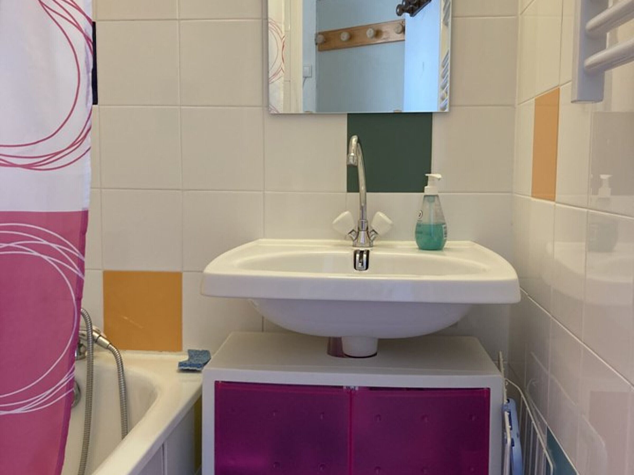 A bathroom with a white sink, a mirror above it, and a pink cabinet below.