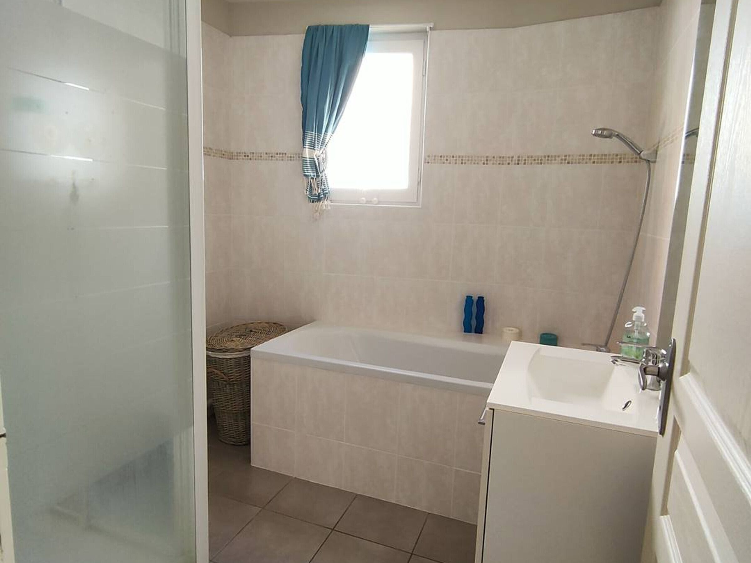 Un baño con bañera, lavamanos y una ventana con cortina azul.