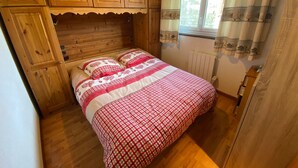 Une pièce chaleureuse en bois, avec un lit, des armoires en bois et une fenêtre avec des rideaux.