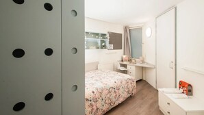 Et soveværelse med en seng, et sminkebord med spejl, en kommode og et klædeskab med runde udskæringer.