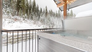 A hot tub on a balcony with a view of a snow-covered forest.