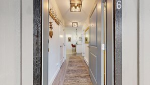 A hallway with a carpet, a door with a number, and a wall-mounted light fixture.