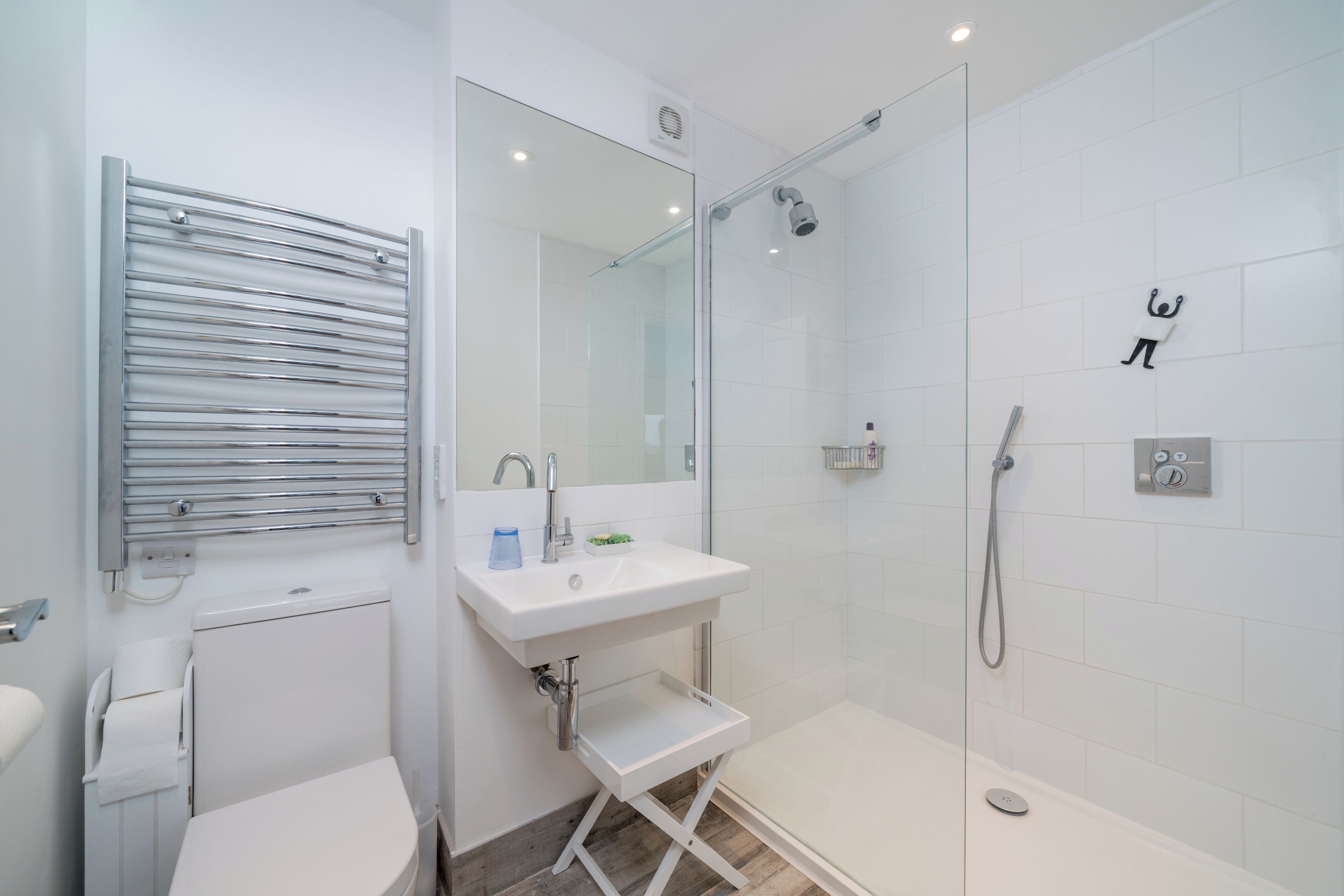 A modern bathroom with a glass-enclosed shower, a white sink with a mirror above it, and a towel rack.