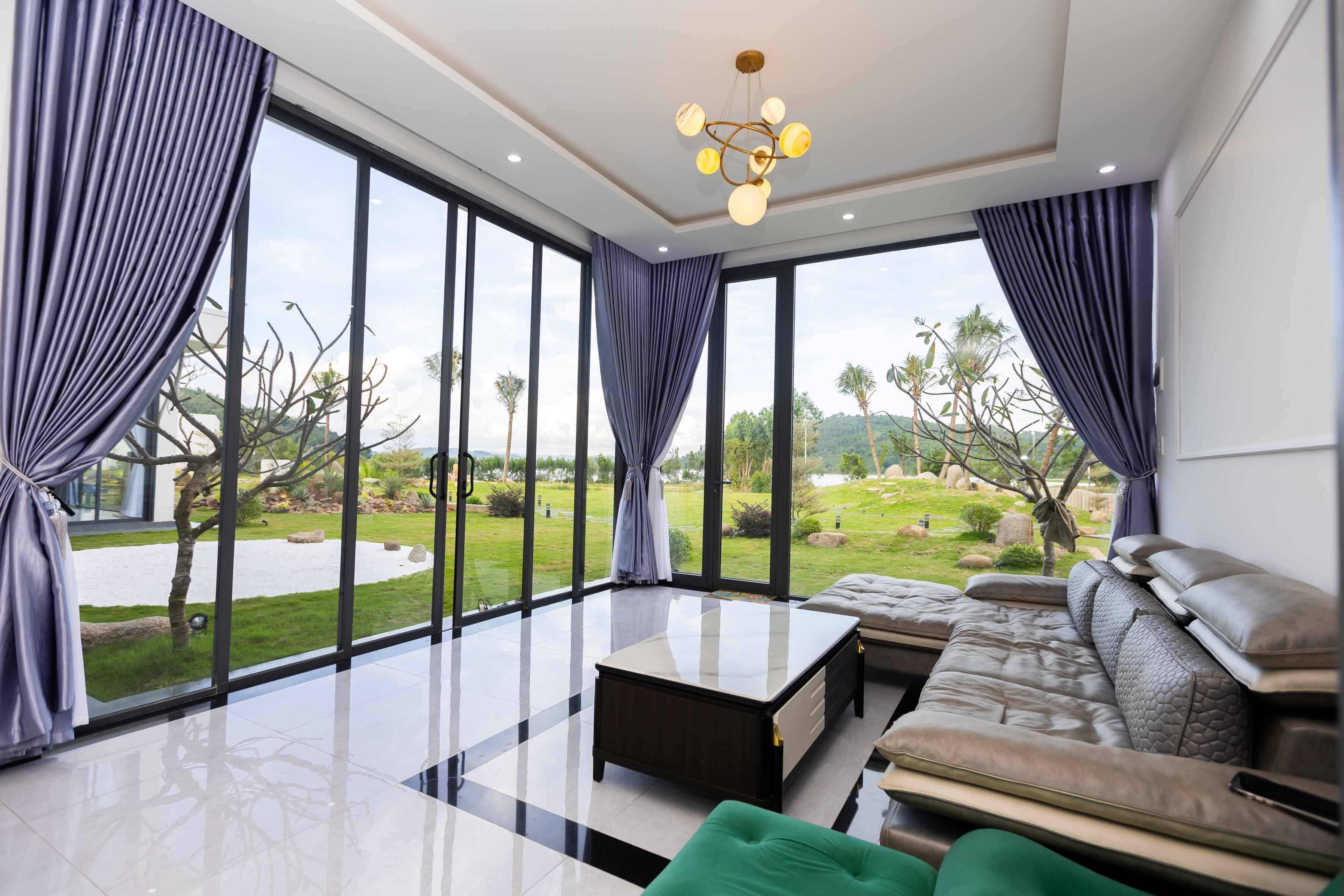 A modern living room with large windows, a sofa, a coffee table, and a chandelier.
