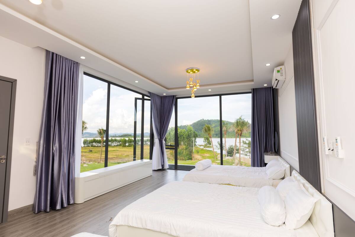 A modern hotel room with a large bed, a view of the outdoors, and a ceiling light fixture.