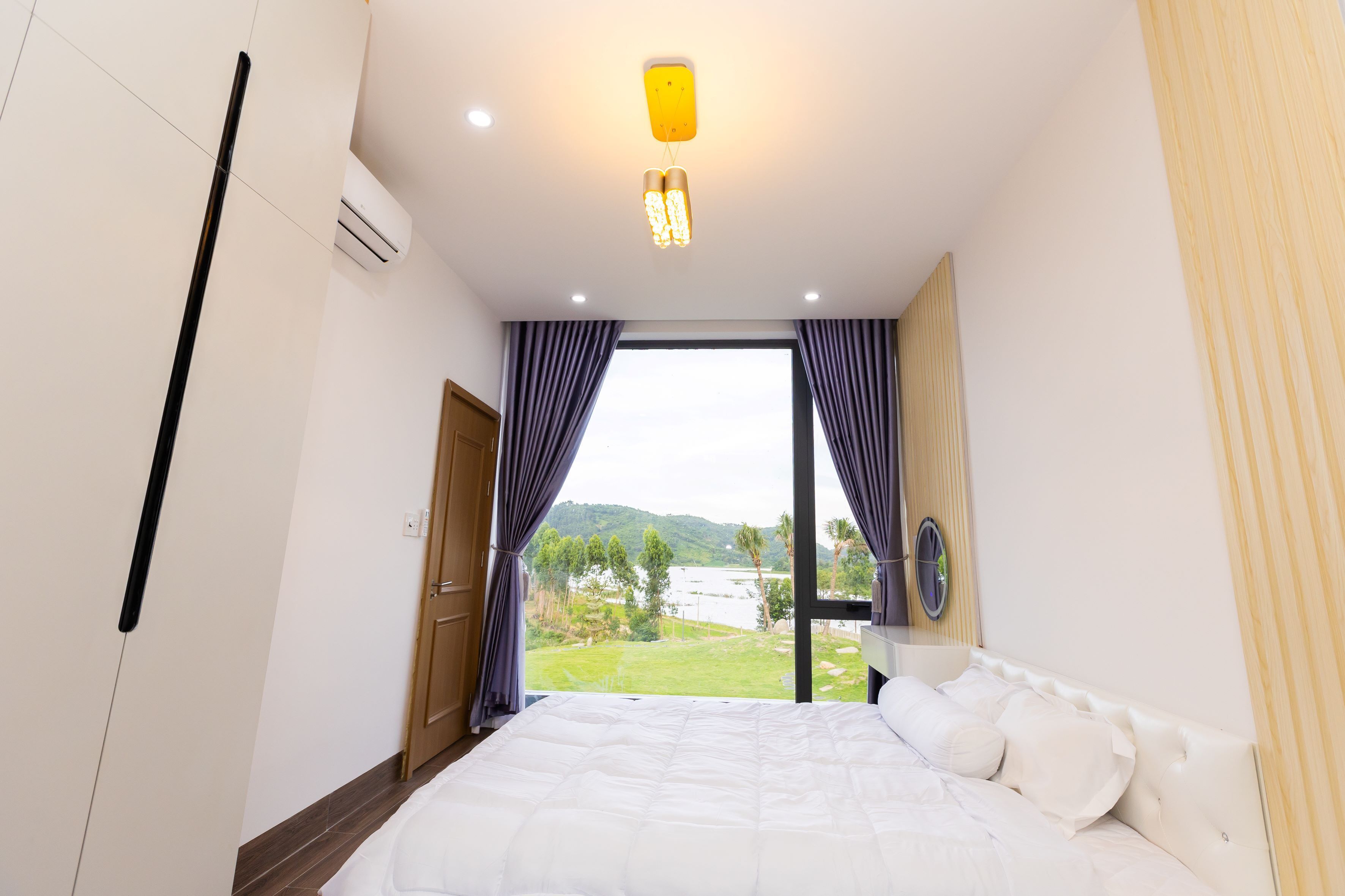 Ein Schlafzimmer mit einem großen Bett, einem Fenster mit Vorhängen und Blick auf einen See und Hügel.