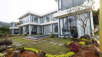 A modern two-story house with large windows, a stone pathway, and a landscaped garden with rocks and shrubs.