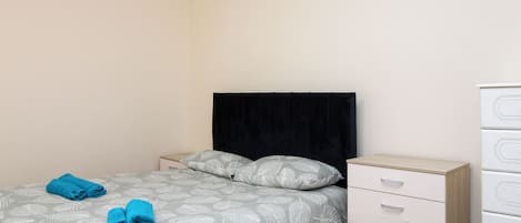 A neatly made bed with a leaf-patterned bedspread and pillows, a white dresser with drawers, and a black headboard.
