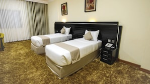 Quarto de hotel com duas camas, uma mesinha de cabeceira com telefone e uma janela grande com cortinas.