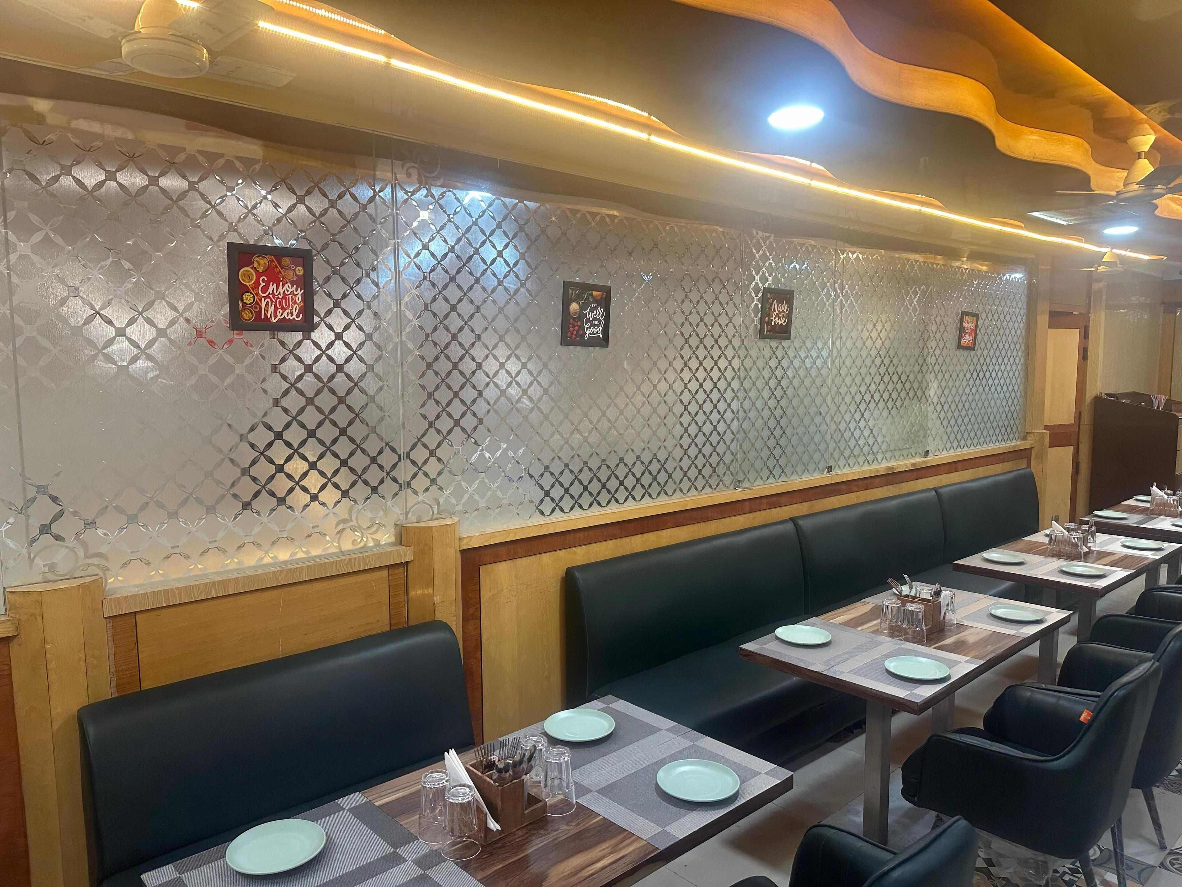 A restaurant interior with long tables, black cushioned booths, and decorative wall panels.