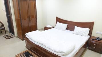 A neatly made bed with white bedding, a wooden wardrobe, and a bedside table with a phone.
