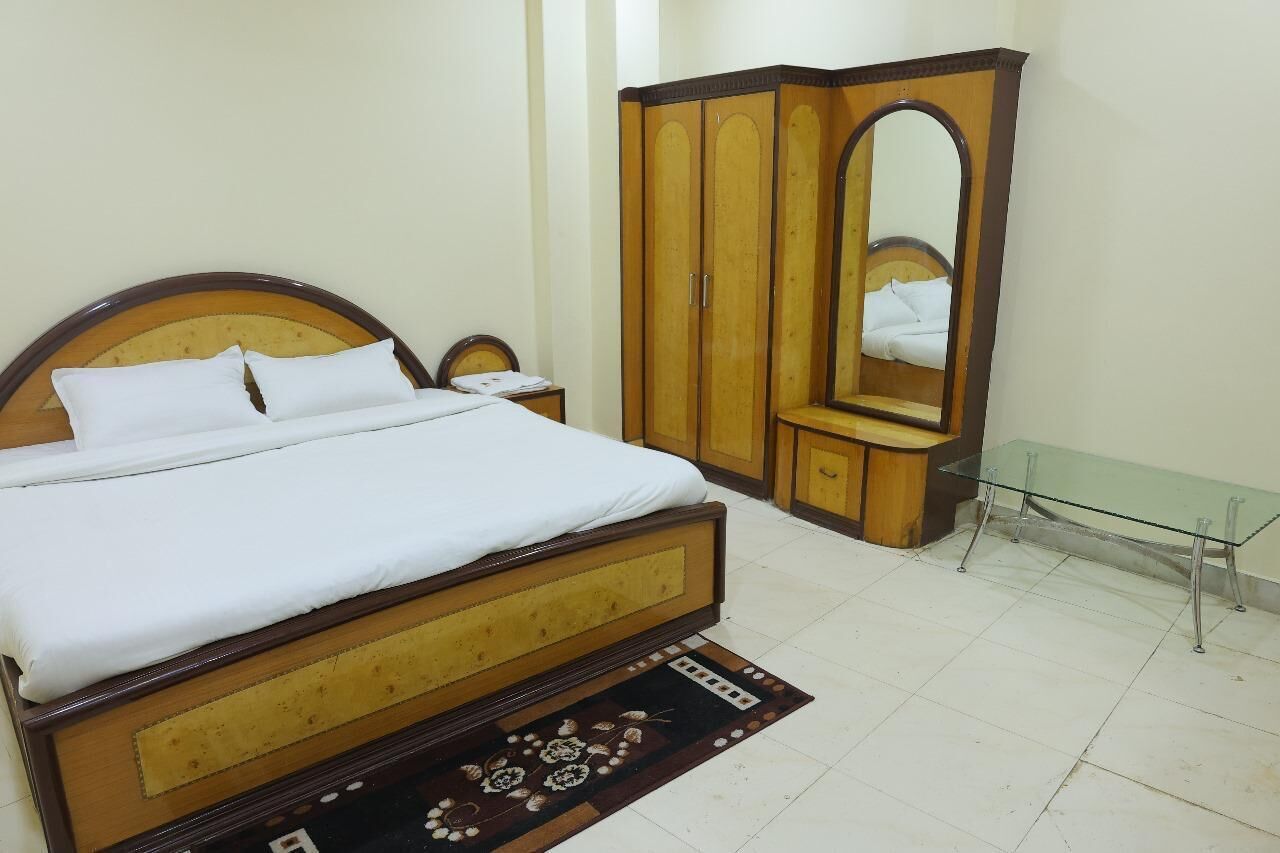 Un dormitorio con una cama de madera, un armario, un espejo y una mesita de cristal.