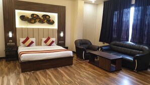 Een hotelkamer met een bed, een slaapbank, een stoel, een bijzettafeltje en een decoratief wandobject.