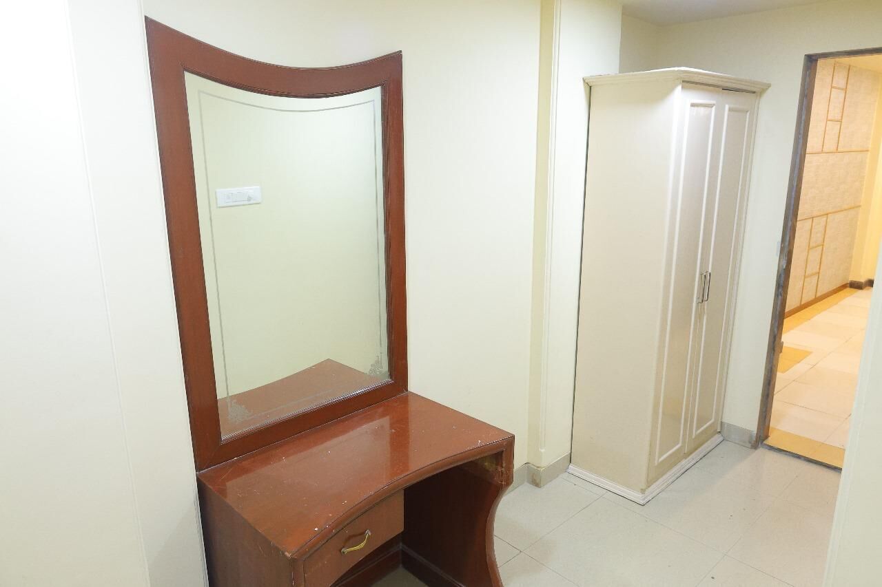 A room with a wooden vanity, a mirror, a white wardrobe, and a tiled floor.