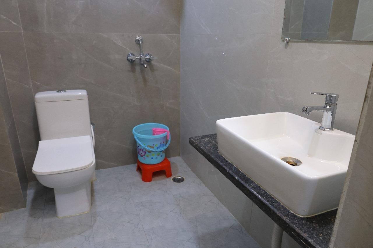 A bathroom with a toilet, a small blue bucket, and a white sink.