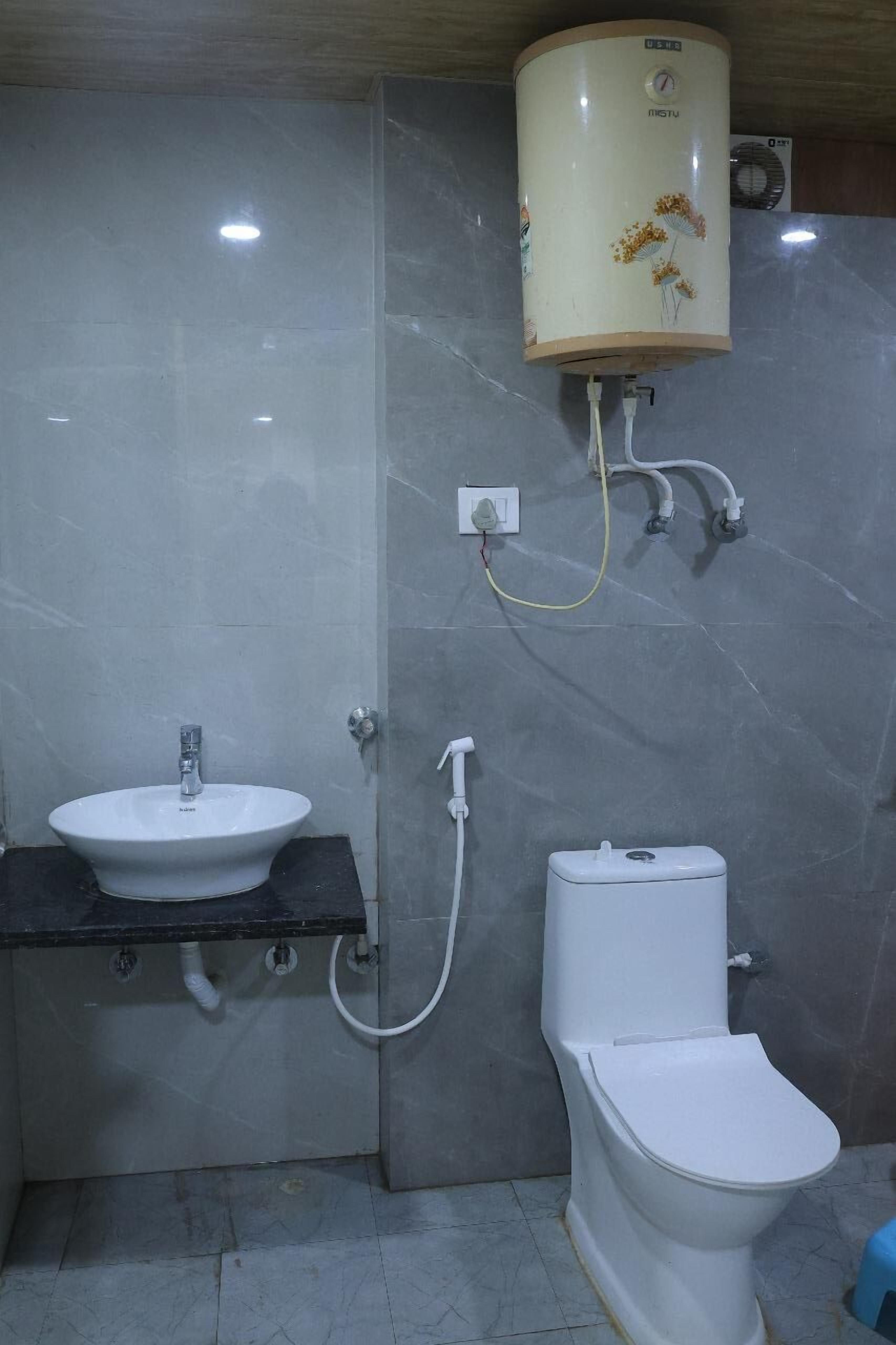 Un baño con lavamanos blanco, inodoro y calentador de agua montado en la pared.