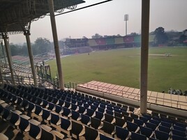 Un estadio vacío con asientos en niveles y un campo de críquet.