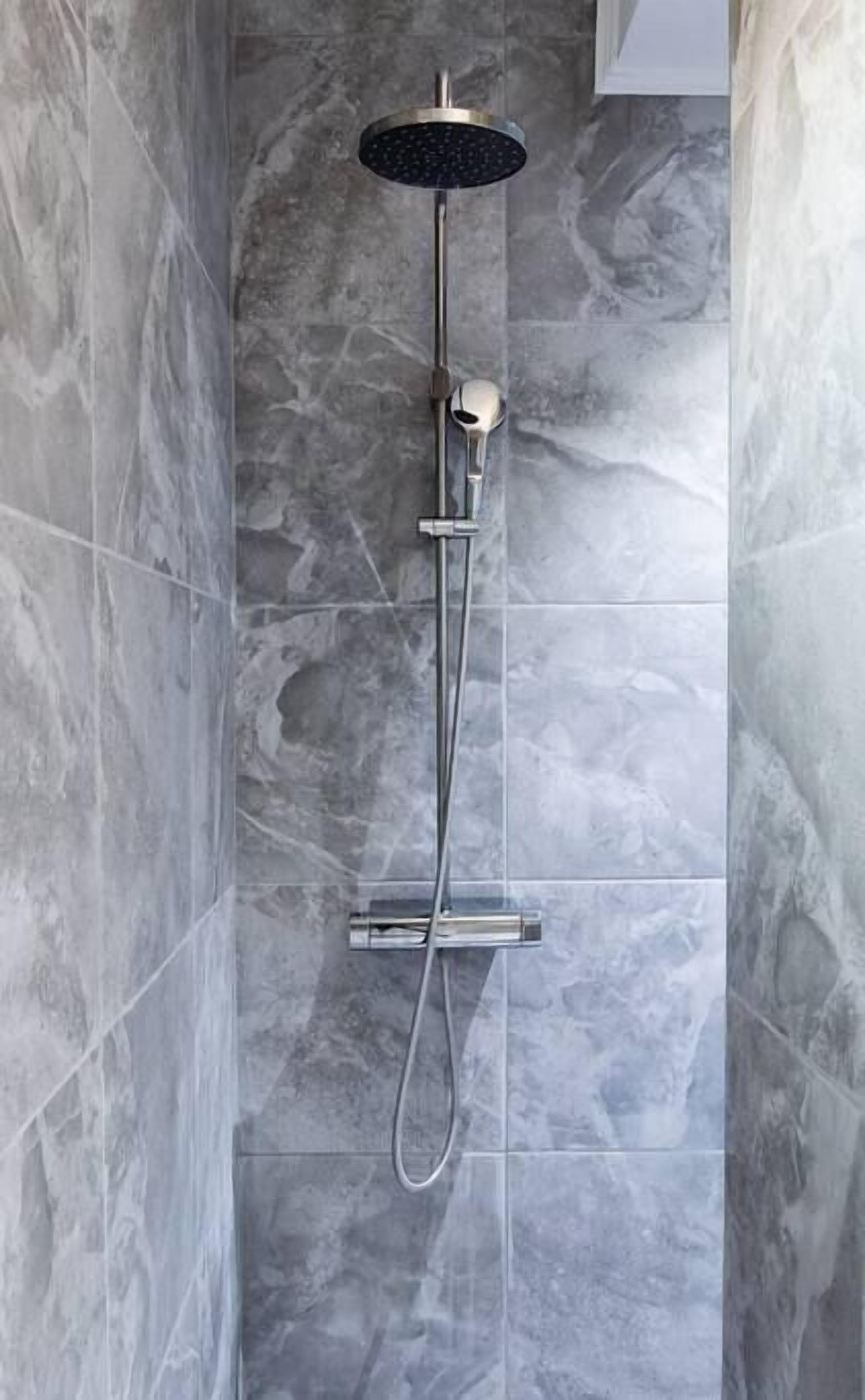Eine moderne Dusche mit Regendusche und Handbrause, vor einer Marmorwand.