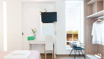 Een hotelkamer met een bed, een bureau met stoel, een aan de muur bevestigde televisie, een raam met uitzicht op groen en een kledingkast met daarin hangende kleding.