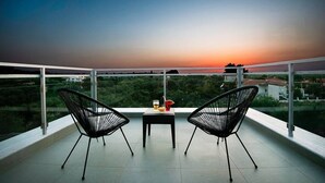 Un balcon avec deux chaises noires, une petite table avec une boisson, et une vue sur le coucher de soleil.