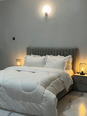 Relax in a serene bedroom with a neatly made bed, grey headboard, and bedside tables with wall-mounted lamps.