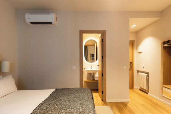 A bedroom with a bed, a bedside lamp, an air conditioner, and a view into a bathroom with a sink and mirror. - Colectia Stays Gran Vía (Madrid)