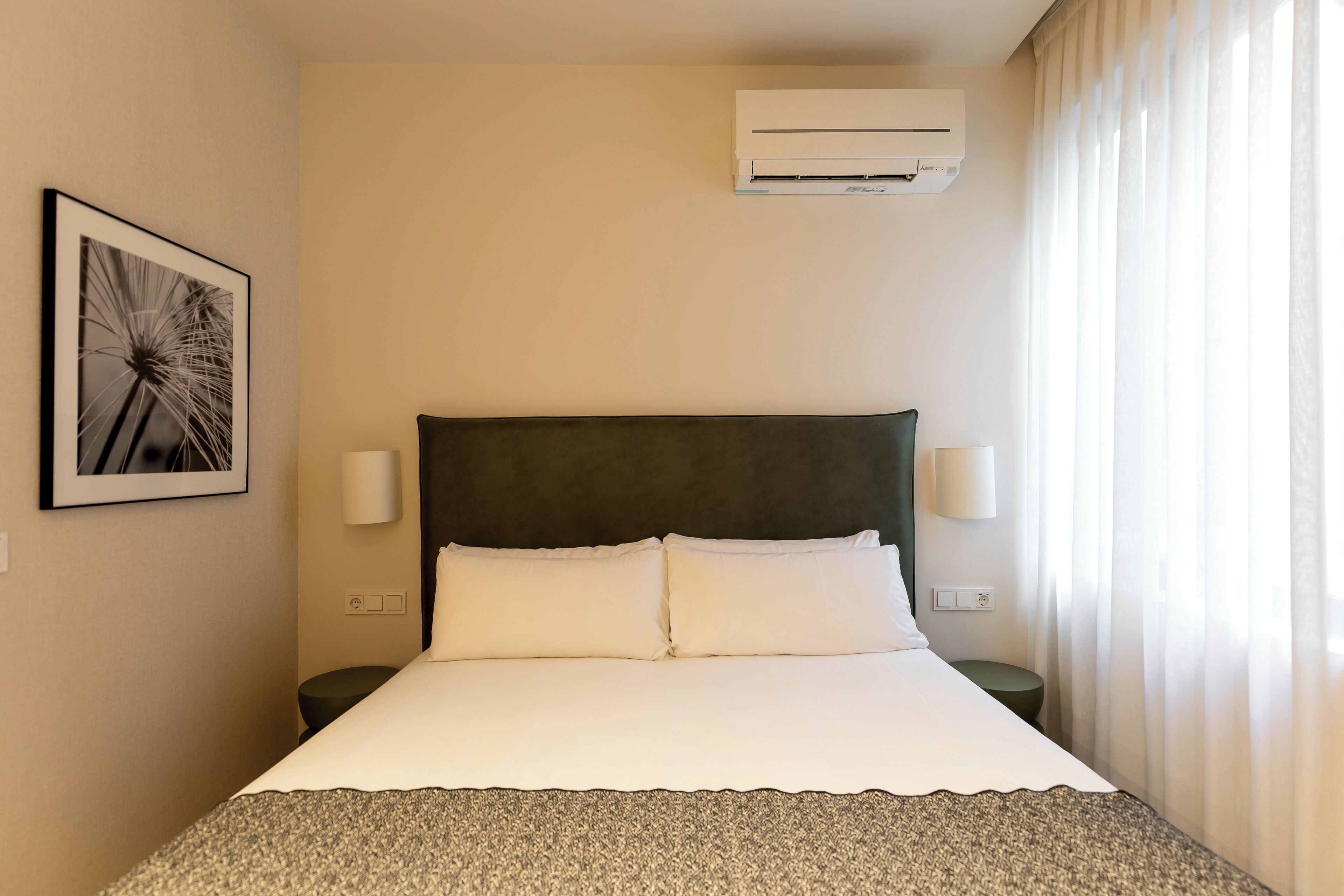 Habitación de hotel con cama, dos lámparas de noche, aire acondicionado y un cuadro en la pared.