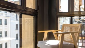 A wooden chair with a woven backrest and cushion, positioned near a window with a view of buildings. - Colectia Stays Gran Vía (Madrid)