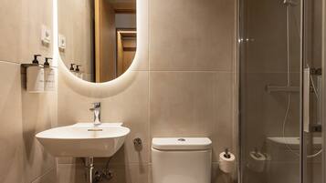 Une salle de bain moderne avec un miroir incurvé, un lavabo, des toilettes et une douche à parois de verre.