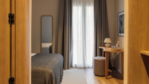 A hotel room with a bed, a bedside table with a lamp, a small stool, a mirror, and a window with curtains. - Colectia Stays Gran Vía (Madrid)